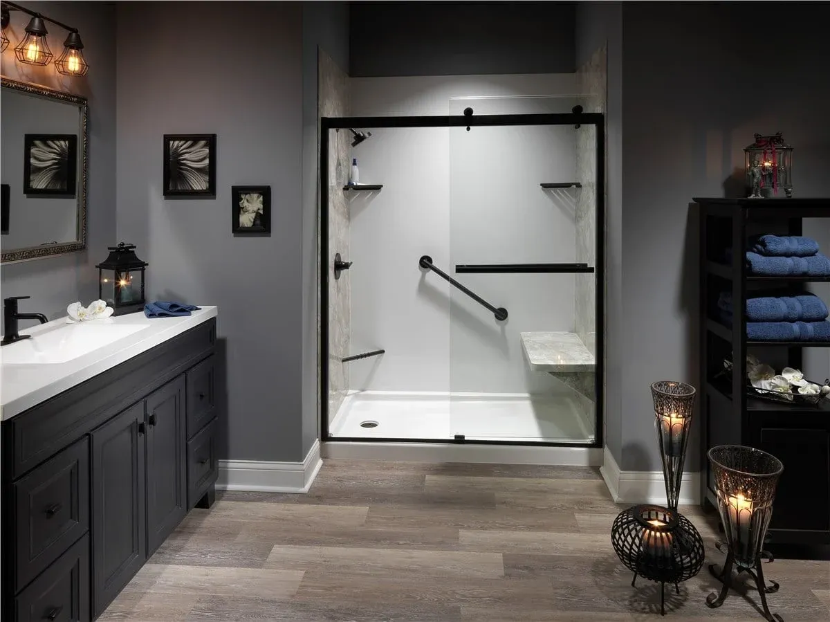 Modern bathroom with sliding glass shower door, black vanity with white countertop, framed wall art, and decorative lighting fixtures