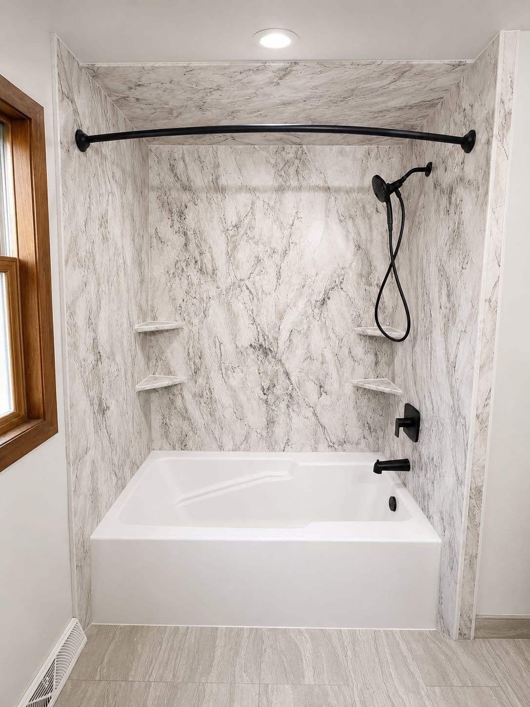 Modern bathtub enclosure with marble-look walls, black curved shower rod and fixtures, white bathtub, and two white shelves