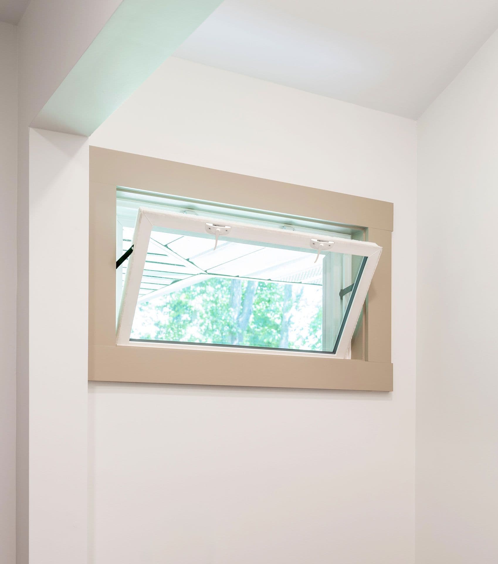 Awning window set in beige-framed opening on white wall, showing green foliage outside