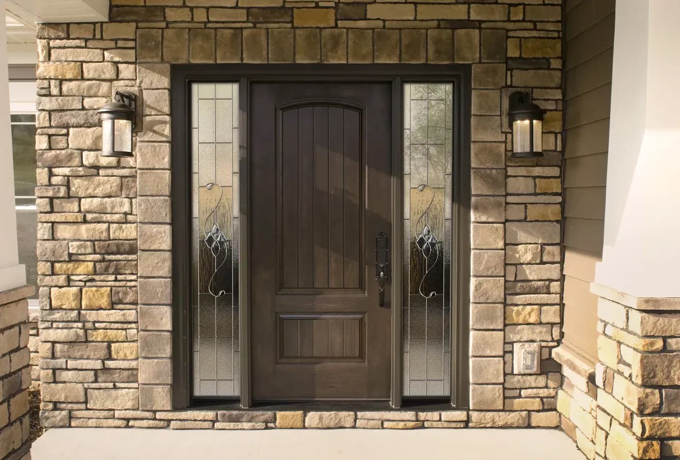 Dark wood front entry door with decorative glass sidelights, black hardware, and stone exterior surround.