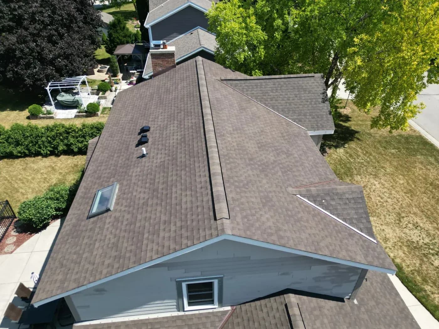 Aerial view of a residential home with a brown asphalt shingle roof, skylight, vents, and multiple rooflines.