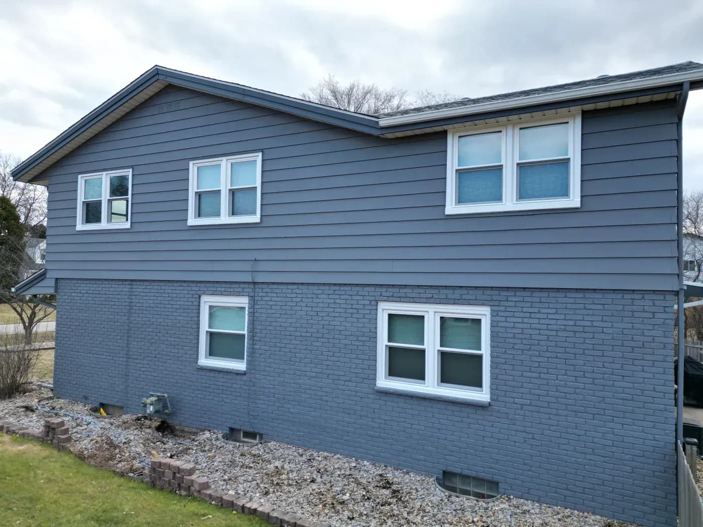 Two-story home exterior with blue-gray siding, painted brick, and multiple white-framed replacement windows.