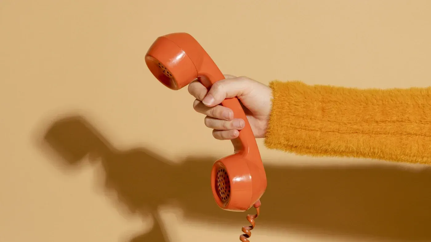 Hand holding an orange vintage telephone receiver against a warm beige background, symbolizing communication and customer service.
