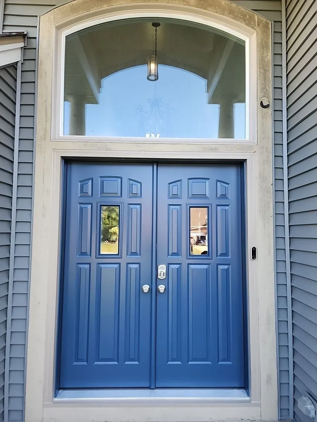 Blue double front entry doors with decorative panels, small glass inserts, silver hardware, and a large arched transom window.