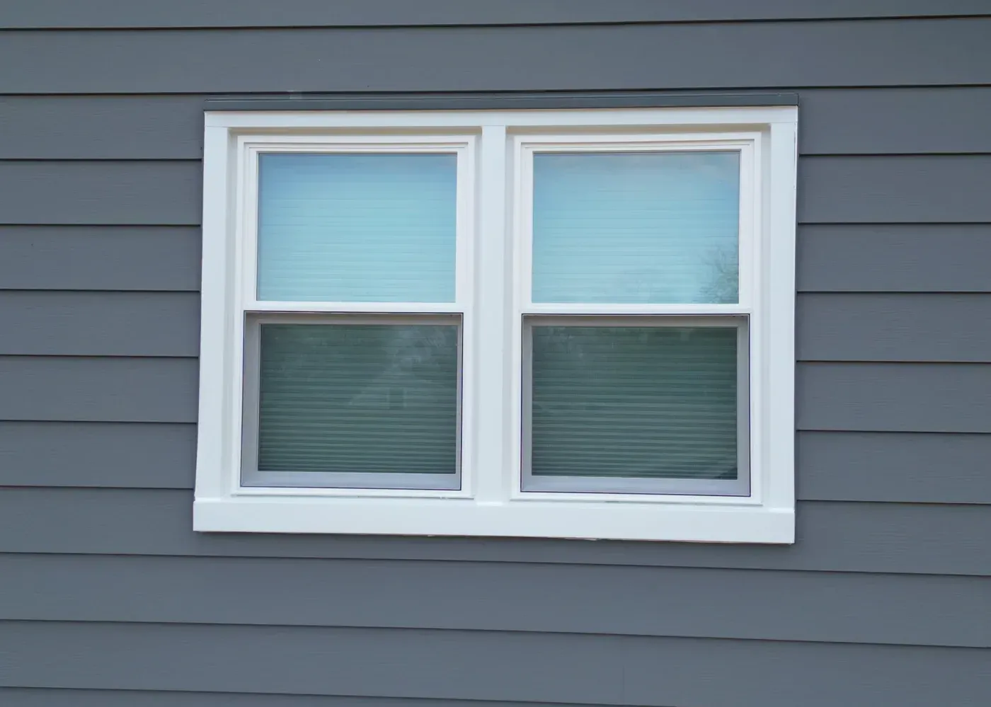 Two white vinyl replacement windows with white trim installed on a home with gray siding in Sussex, Wisconsin.