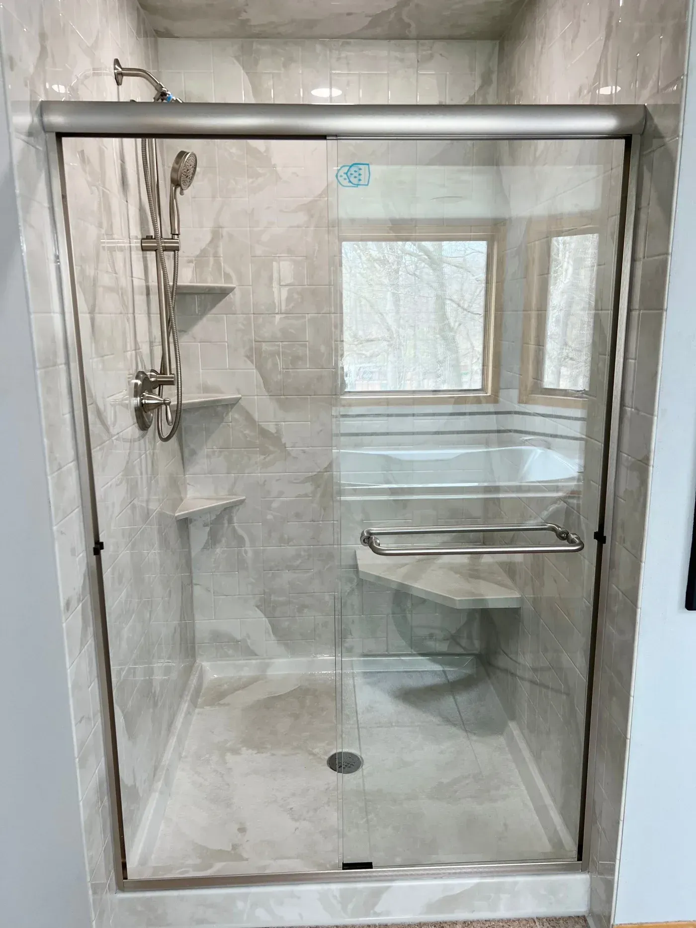 Walk-in shower replacement with marble-look wall panels, glass sliding doors, built-in corner shelves, bench seat, and handheld showerhead in Sussex, Wisconsin.