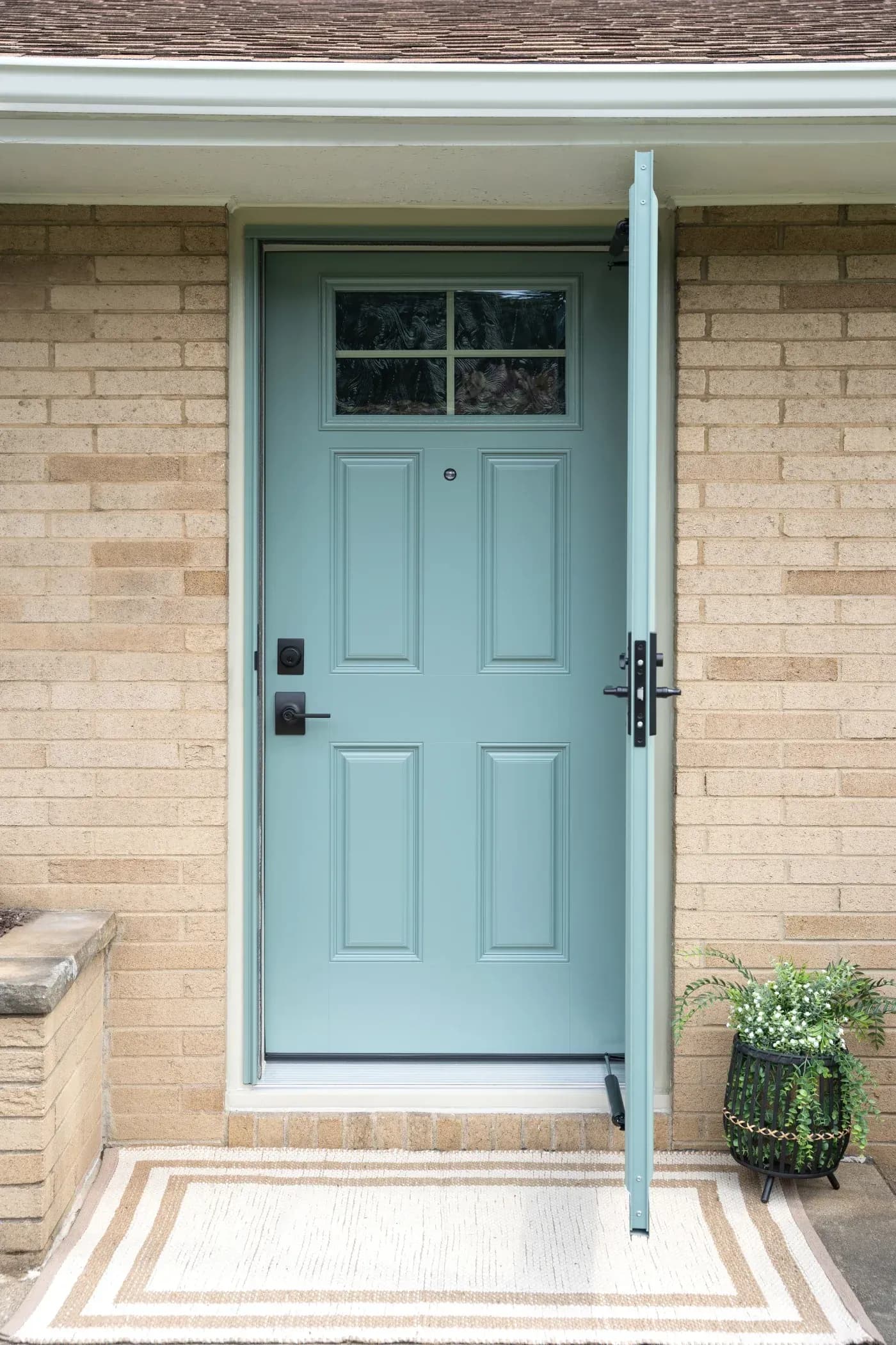 Light blue front entry door with decorative panels, window panes, black hardware, and matching storm door set in a brick exterior.
