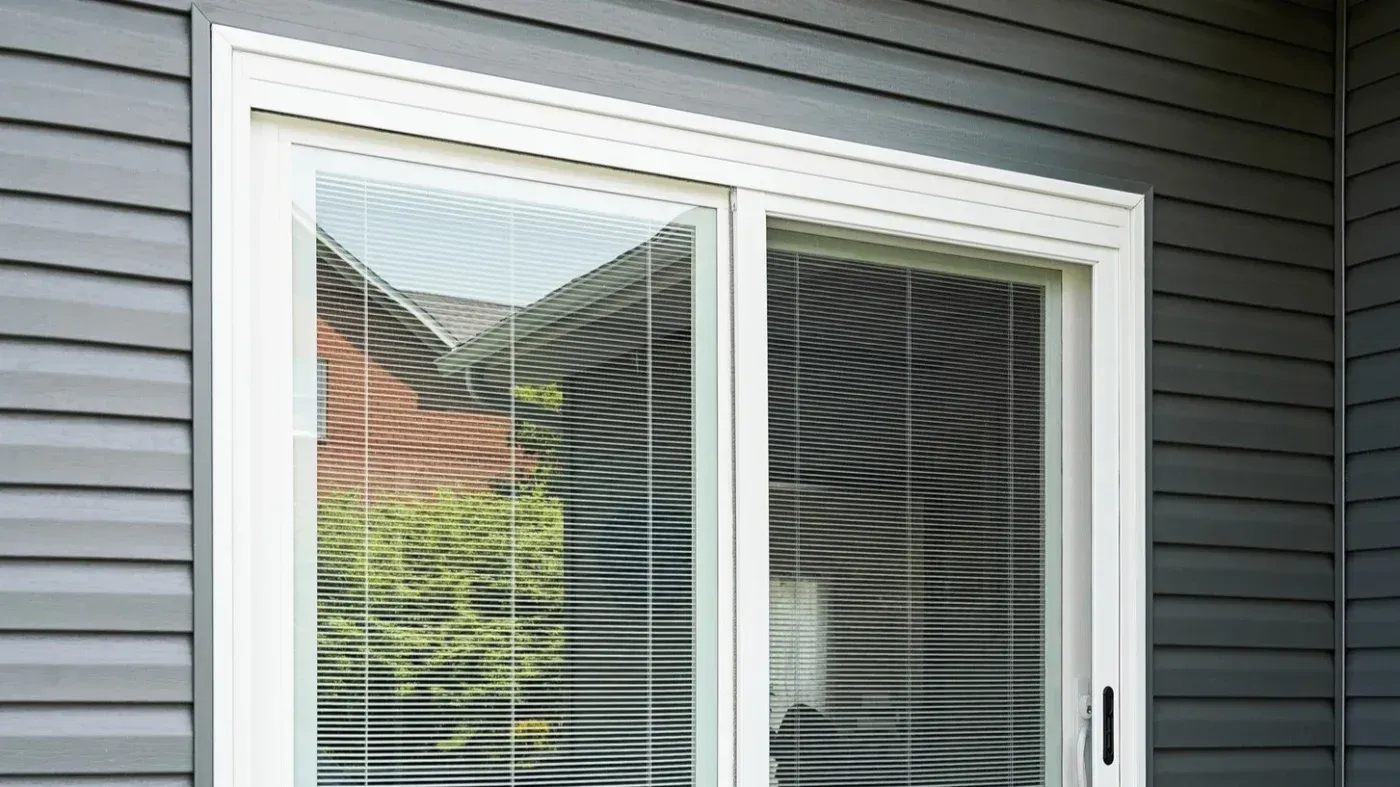White sliding patio door with built-in blinds set in gray horizontal siding.