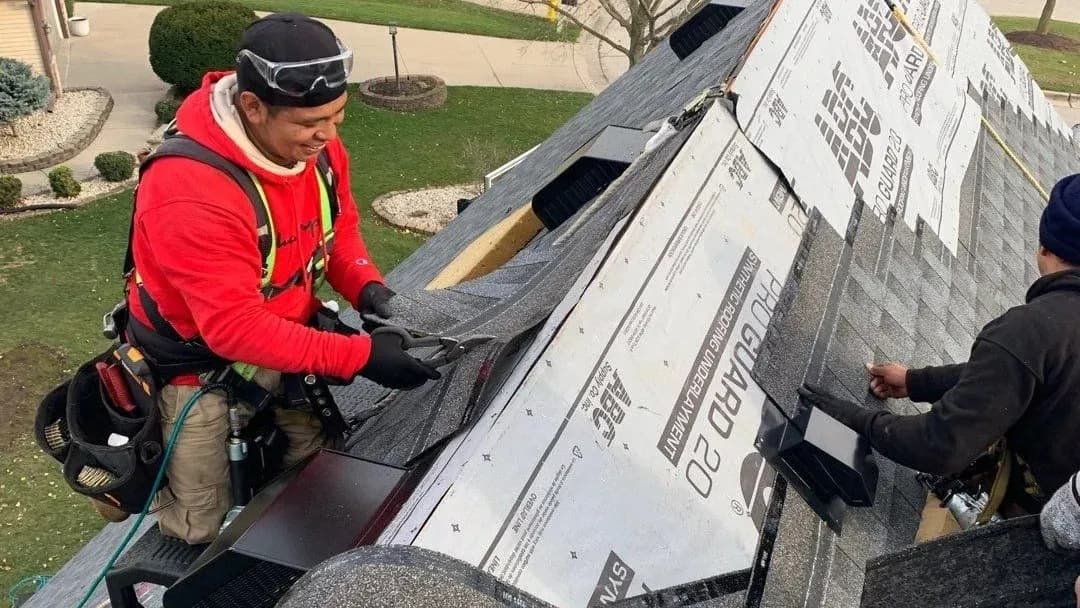 Roofing contractors installing gray asphalt shingles over roof underlayment on a residential home.