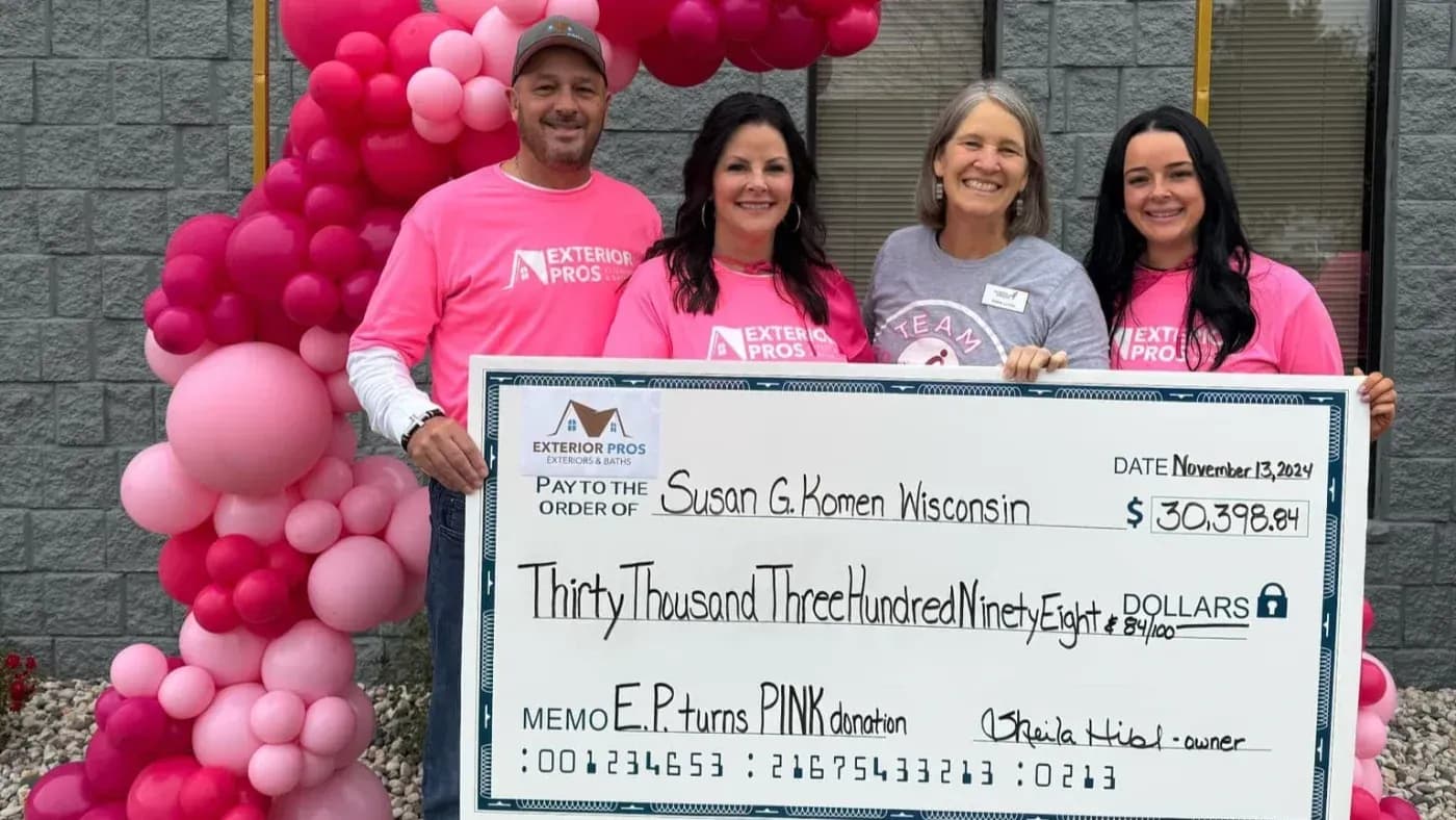 Four people posing with a large charitable donation check for Susan G. Komen, surrounded by pink balloons during an Exterior Pros community event.