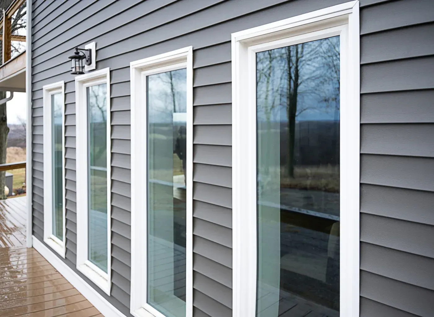 Tall vinyl replacement windows with white trim installed on a home with dark gray siding in Elm Grove, Wisconsin.