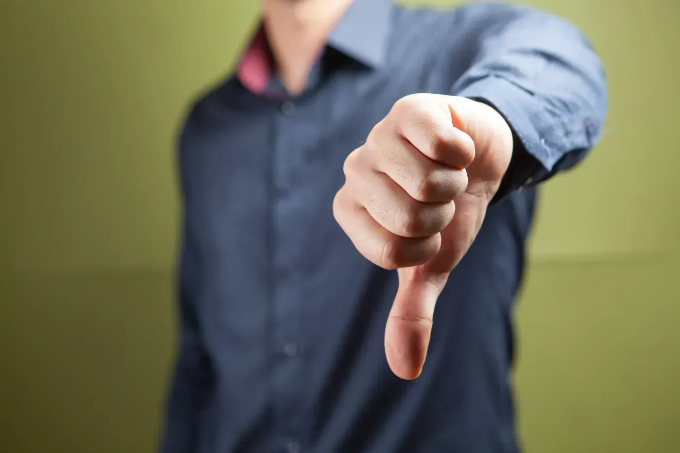 Person giving a thumbs-down gesture against a green background, symbolizing dissatisfaction, disapproval, or a negative experience.
