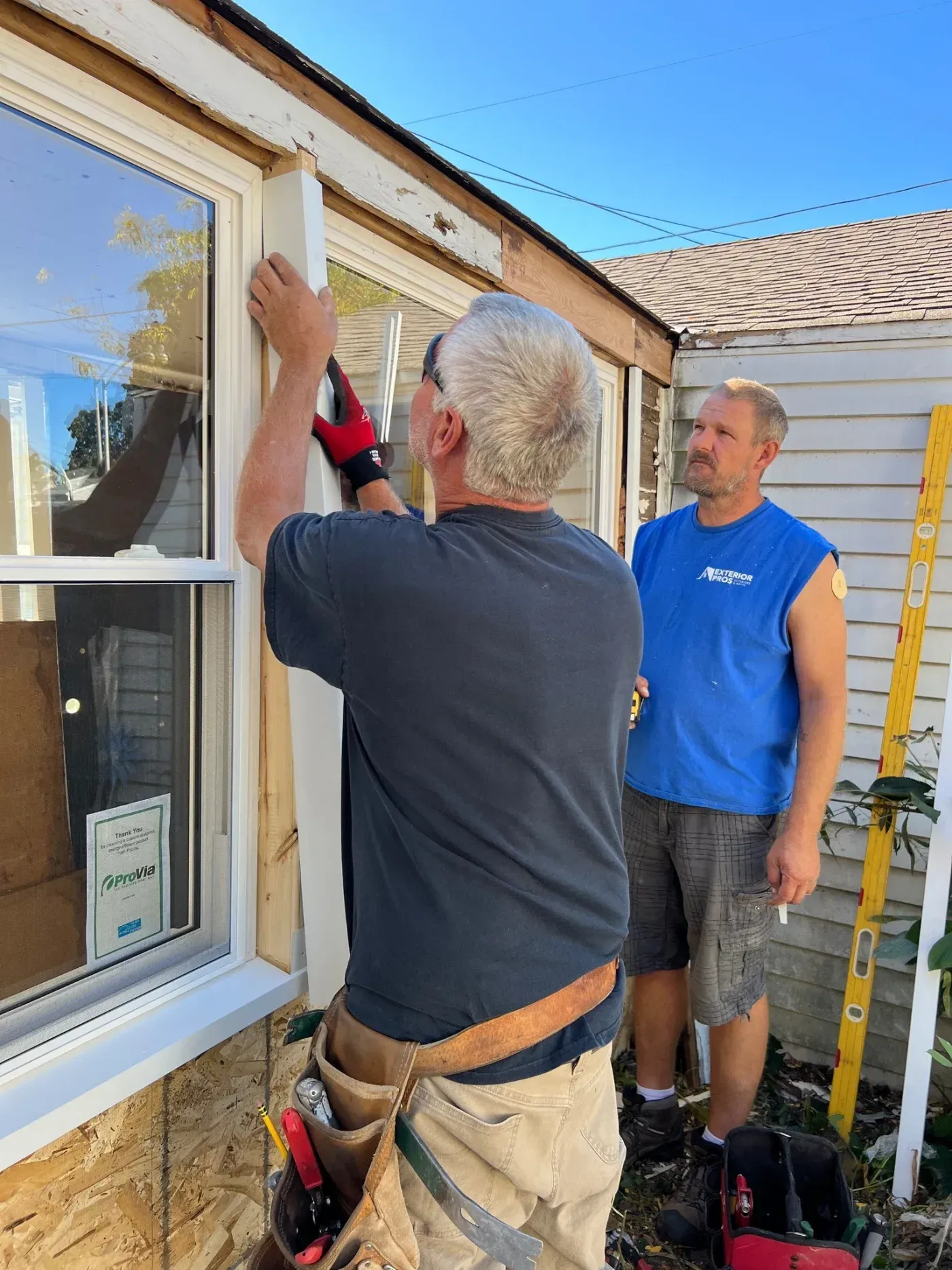 Exterior Pros installers fitting white trim around new vinyl replacement windows in Pewaukee, Wisconsin.