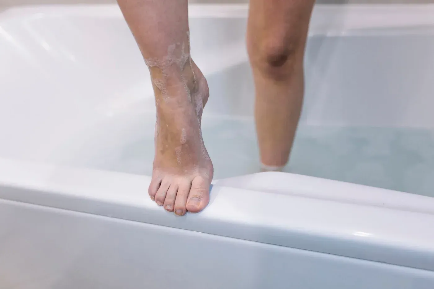 Person stepping over the low edge of a white bathtub, highlighting easy access and bathroom safety in Belgium, Wisconsin.