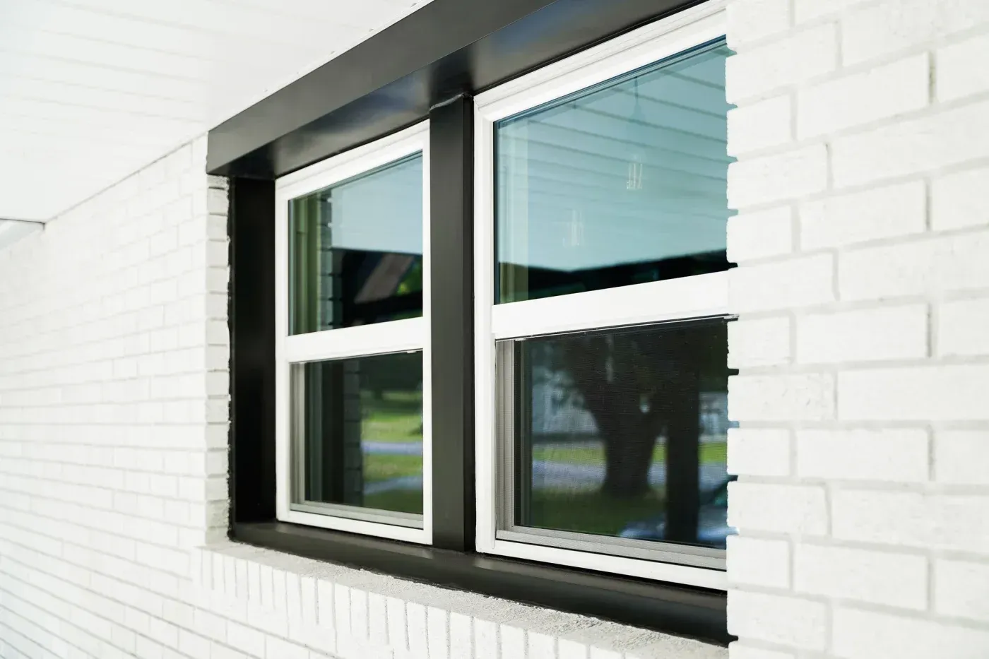 White vinyl replacement windows with black exterior trim installed on a white brick home in Ashippun, Wisconsin.