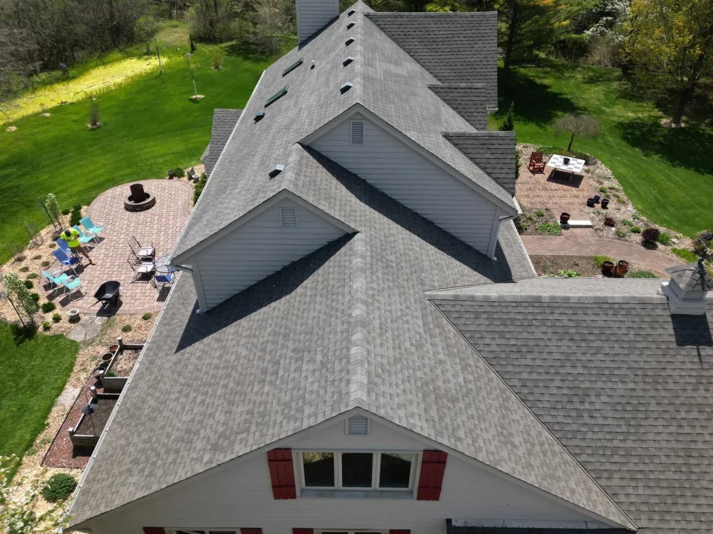 Aerial view of a large home with a complex gray asphalt shingle roof, skylights, and landscaped patio areas.