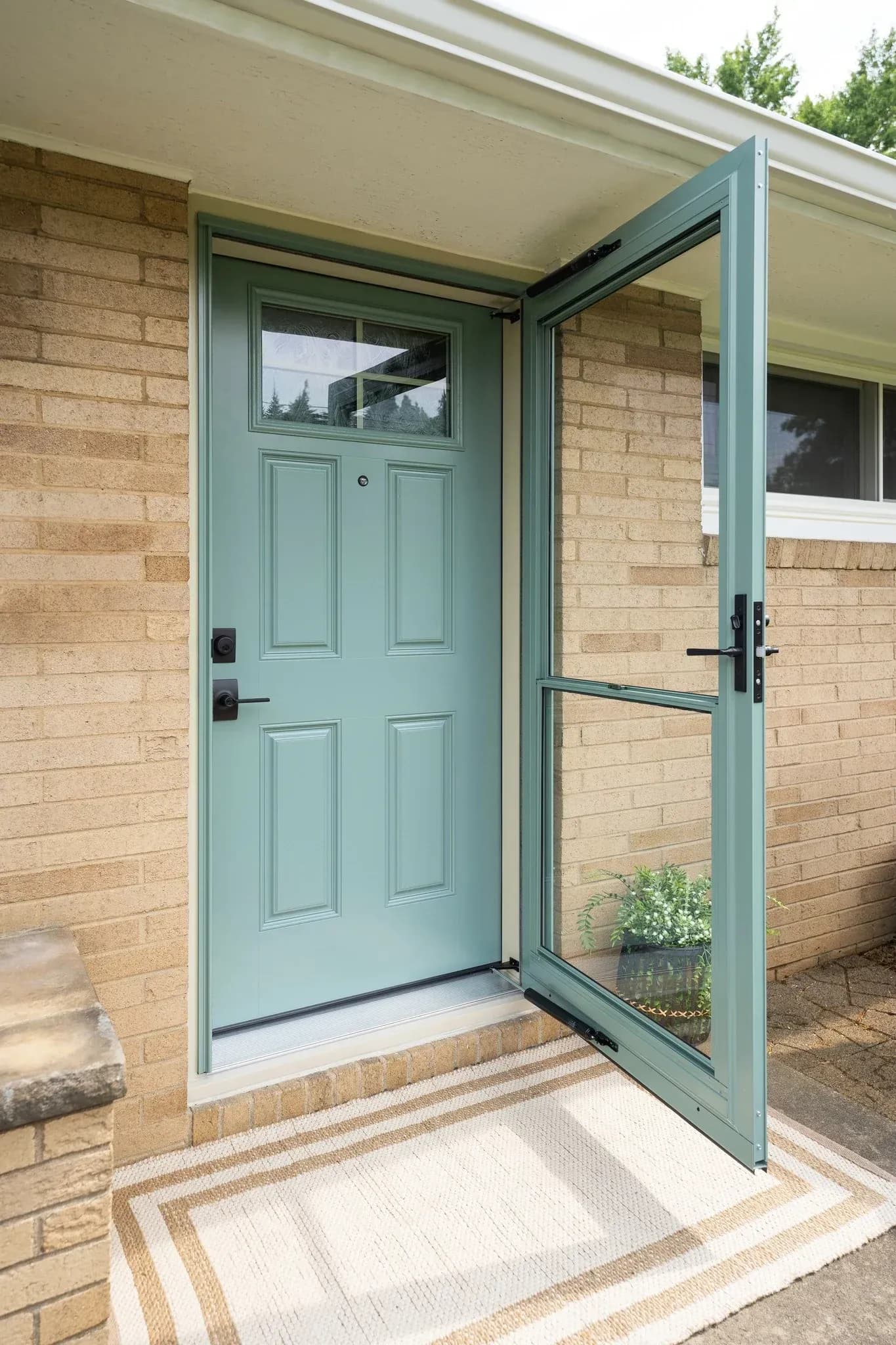 Light blue front entry door with decorative panels and window, paired with a matching open storm door on a brick home exterior.