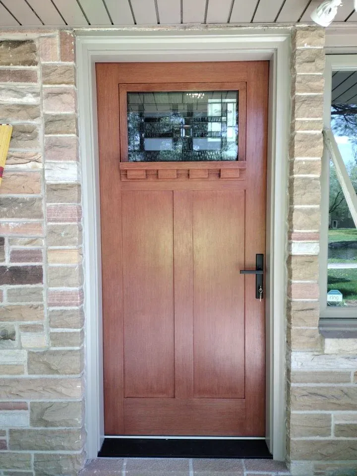 Wooden entry door with textured glass window at top, two panels below, black lever handle, set in stone archway with white trim