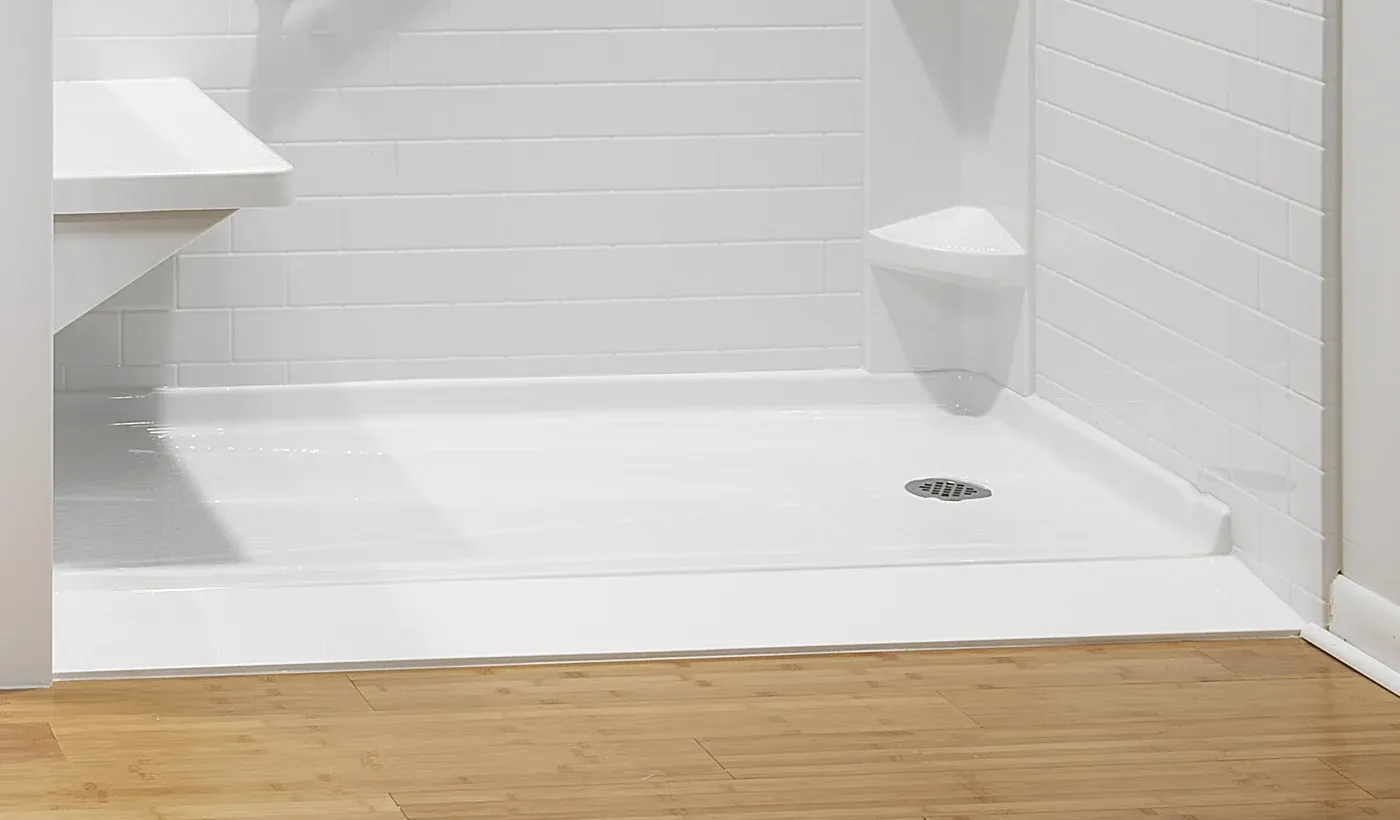 Interior view of an accessible walk-in shower featuring a low-threshold slip-resistant white base, white subway tile wall surround, built-in corner shelves, and a fold-down shower seat.