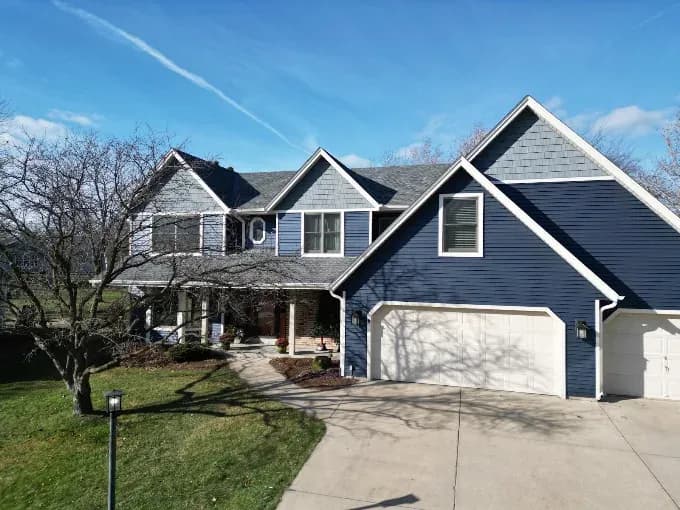imgi_1_AHRPTWlvHRQGq3fBG_xJqsJu3lLI.webp Exterior view of a large multi-gabled home featuring deep navy blue horizontal siding on the lower level, lighter slate-grey shake siding accents on the upper gable peaks, crisp white trim, and white garage doors under a grey shingle roof.
